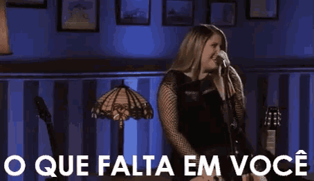 a woman is singing into a microphone in front of a sign that says o que falta em voce