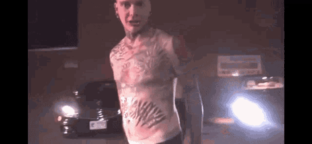 a man with a tattoo on his chest is standing in front of a car in a parking lot .