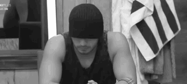 a black and white photo of a man wearing a black hat and a tank top .
