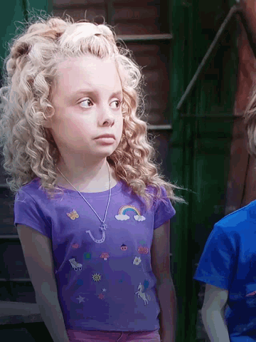 a little girl with curly hair is wearing a purple shirt with a rainbow and a question mark on it