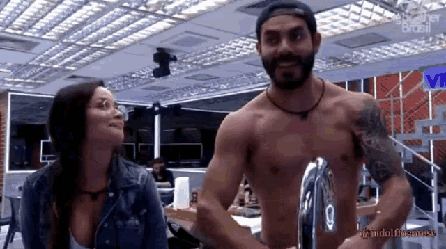 a man without a shirt is standing next to a woman in a kitchen