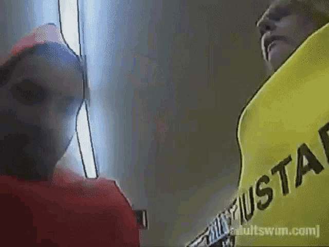 a man in a red hat is standing next to a woman in a yellow vest that says adultswim.com on it .