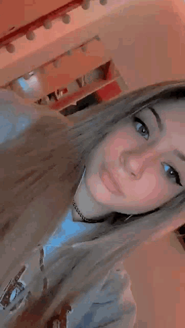 a girl with long hair is taking a selfie in a room with a shelf in the background .