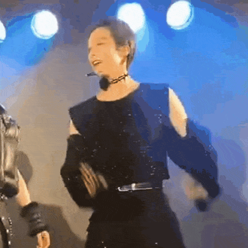 a man in a black dress is dancing on a stage with a microphone .