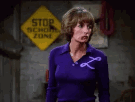 a woman in a purple shirt is standing in front of a yellow stop sign
