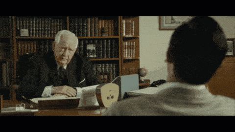 a man in a suit sits at a desk with a clock on it
