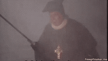 a man in a black robe is holding a sword in his hand in a foggy room .