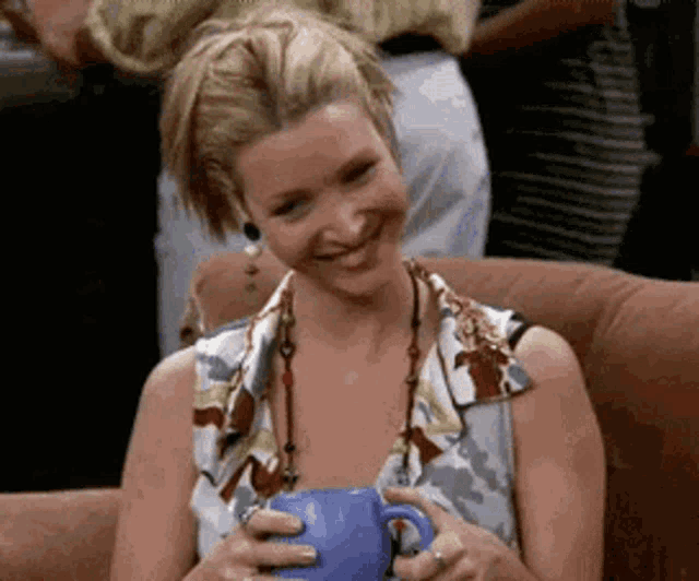 a woman is sitting on a couch holding a blue coffee mug and smiling .