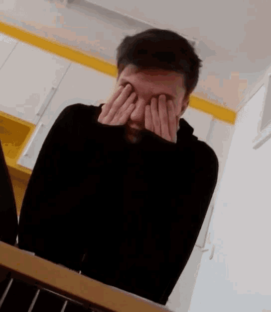 a man covering his eyes with his hands in front of a laptop