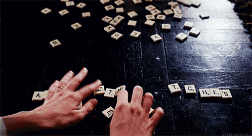 a person is playing scrabble on a wooden table and the letters a t c h e s are visible