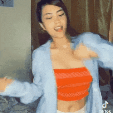 a woman wearing a blue shirt and an orange crop top is dancing in a bedroom .