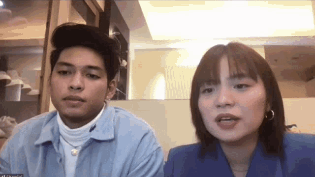 a man and a woman are sitting next to each other on a video call . the woman is wearing a blue jacket .