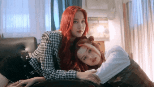 two women with red hair are laying next to each other on a couch in a living room .