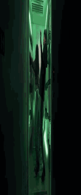 a man in a black hoodie is laying on the floor in a dark room with green lights behind him .
