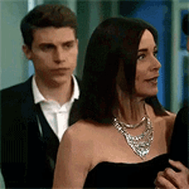 a man and a woman are standing next to each other in a room . the woman is wearing a necklace .