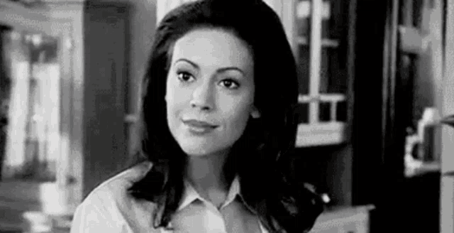 a black and white photo of a woman standing in a kitchen looking at the camera .