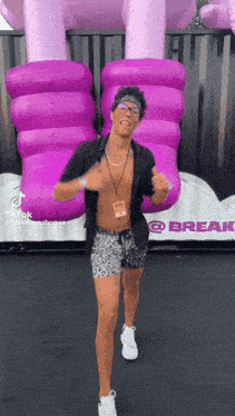 a shirtless man is dancing in front of a giant purple inflatable elephant