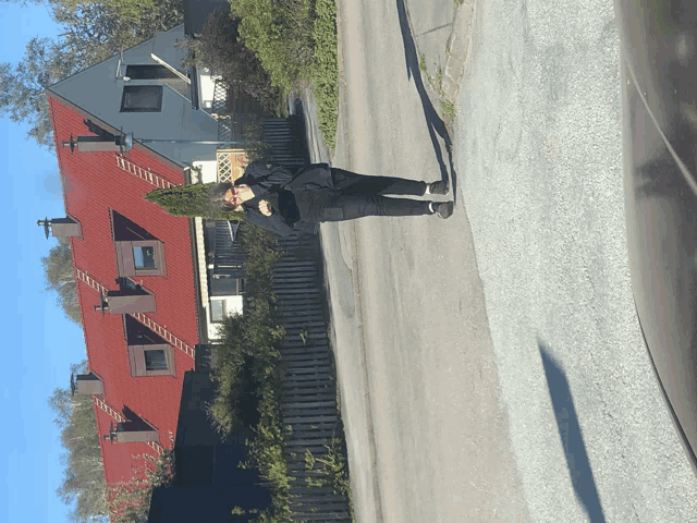 a person standing on the side of the road in front of a building with a red roof
