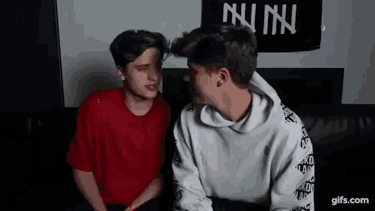 two boys are sitting next to each other on a couch and looking at each other .
