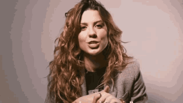 a woman with curly red hair is wearing a plaid jacket