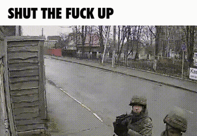 two soldiers are standing on the side of a street with the words shut the fuck up below them