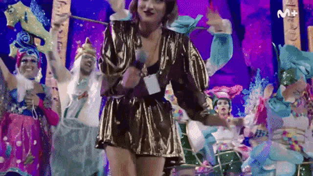a woman in a gold dress is singing into a microphone in front of a crowd