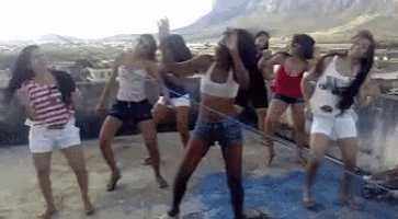 a group of young women are dancing on a rooftop with mountains in the background .