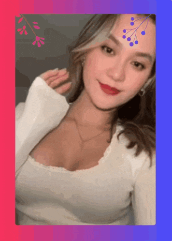 a woman in a white top with a flower on her forehead looks at the camera