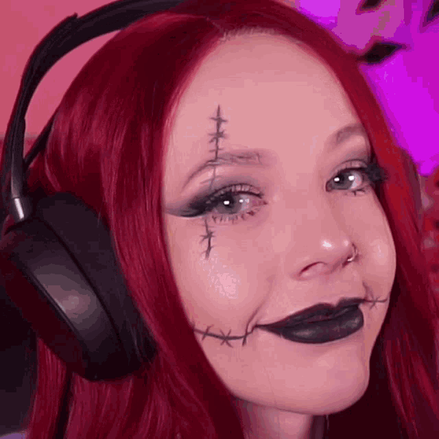 a woman with red hair and black lipstick is wearing headphones and has stitches on her face .