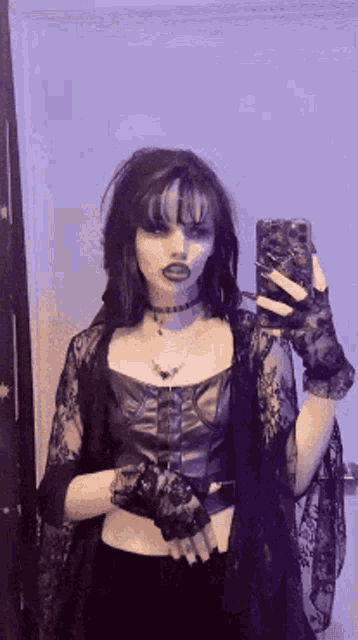 a woman is taking a selfie in front of a mirror while wearing a gothic outfit .
