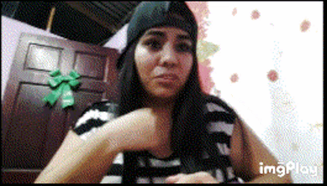 a woman wearing a black beanie and a striped shirt is sitting in front of a door with a green bow on it
