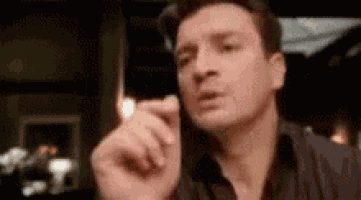 a man is smoking a cigarette in a dark room and pointing at the camera .