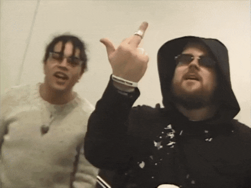 a man wearing a hoodie and sunglasses giving the middle finger