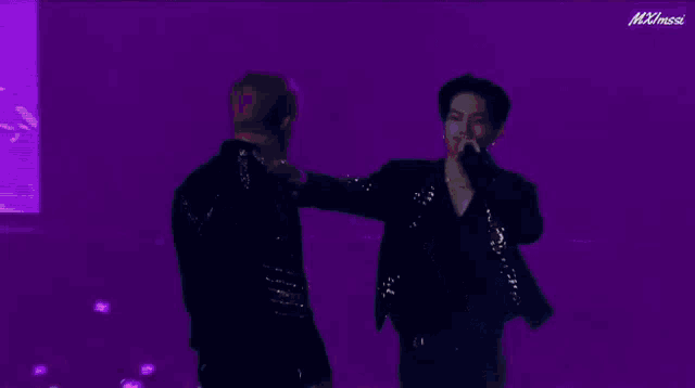 a man with pink hair is singing into a microphone while another man looks on .