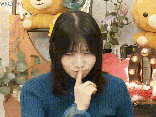 a woman in a blue sweater holds her finger to her lips in front of a sign that says exit