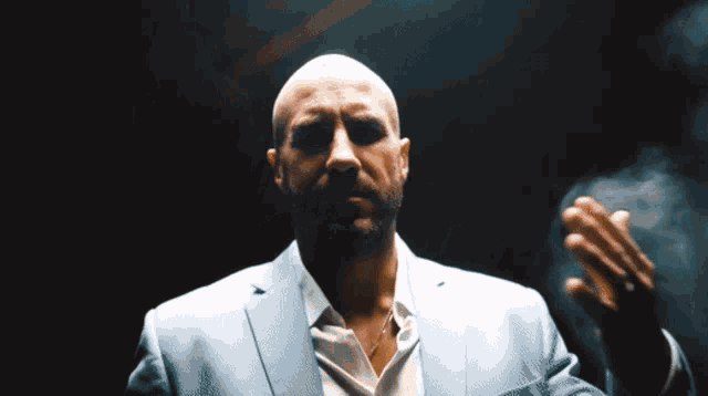 a bald man in a suit and white shirt holds his hand out