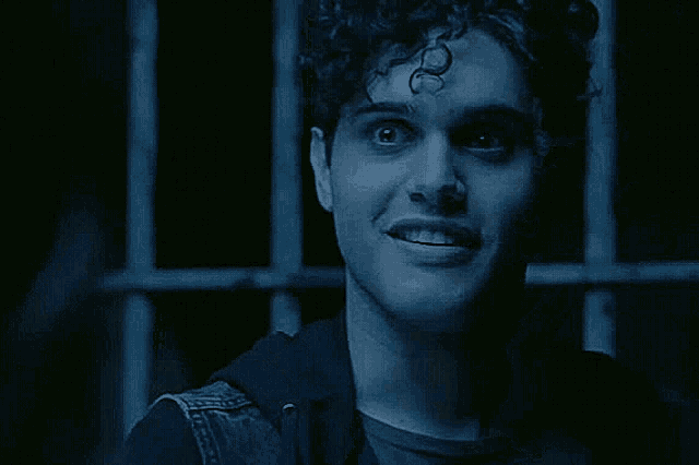 a man with curly hair is standing in a dark room looking at the camera .