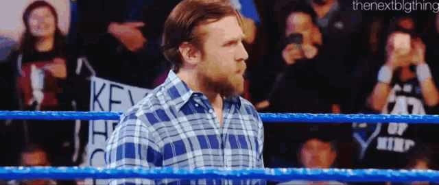 a man in a plaid shirt is standing in a wrestling ring with a crowd watching .