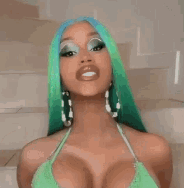 cardi b is wearing a green top and blue hair and making a funny face .