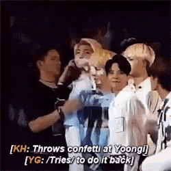 a group of people are standing next to each other and one of them is throwing confetti at yoongi .
