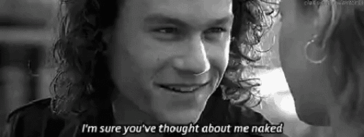 a black and white photo of a man with curly hair smiling and talking to a woman .