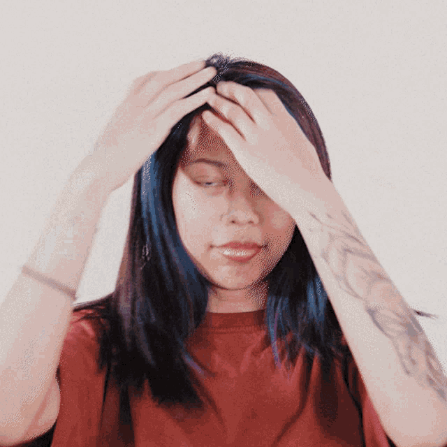 a woman with blue hair and a tattoo on her arm holds her head