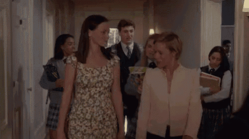 two women are walking down a hallway talking to each other .