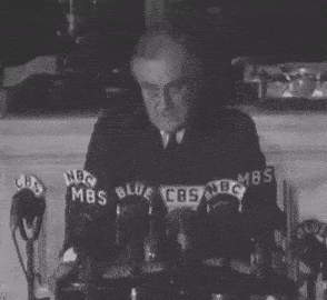 a man in a suit and tie stands in front of microphones with nbc mbs blue and cbs logos on them