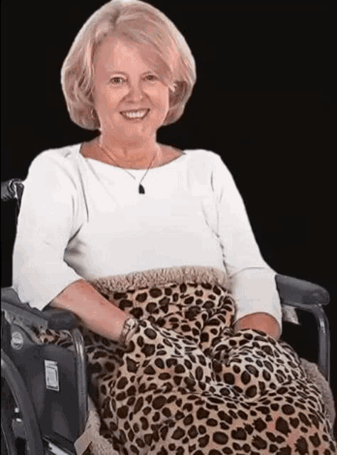 a woman is sitting in a wheelchair with a leopard print blanket on her lap .