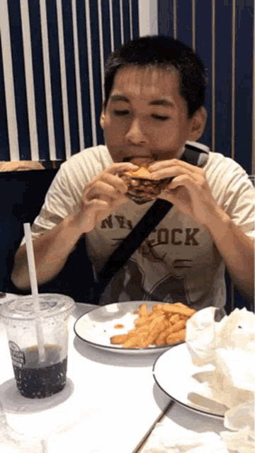 a young boy eating a hamburger with a ny rock shirt on