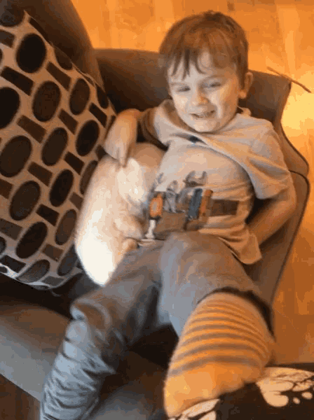 a young boy is sitting in a chair holding a stuffed animal and a pillow