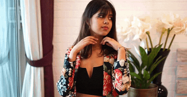 a woman in a floral jacket is standing in front of flowers