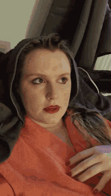 a woman with red lipstick and red nails is wearing a hooded sweatshirt