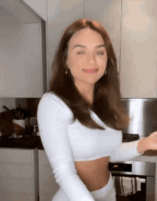 a woman in a white crop top and white pants is standing in a kitchen